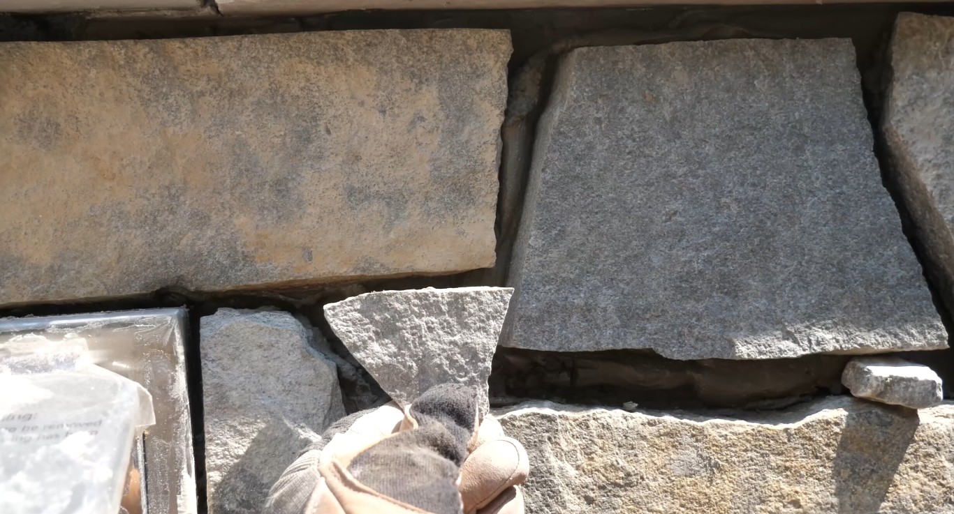 Professional tuckpointing and repointing masonry work showing mason's hands working on stone pavers