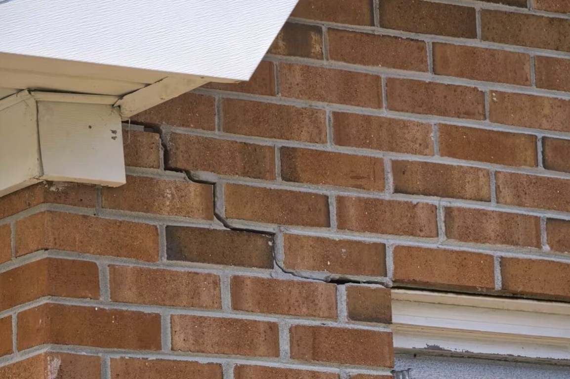 Masonry foundation repair and waterproofing services showing structural brick damage assessment near home exterior